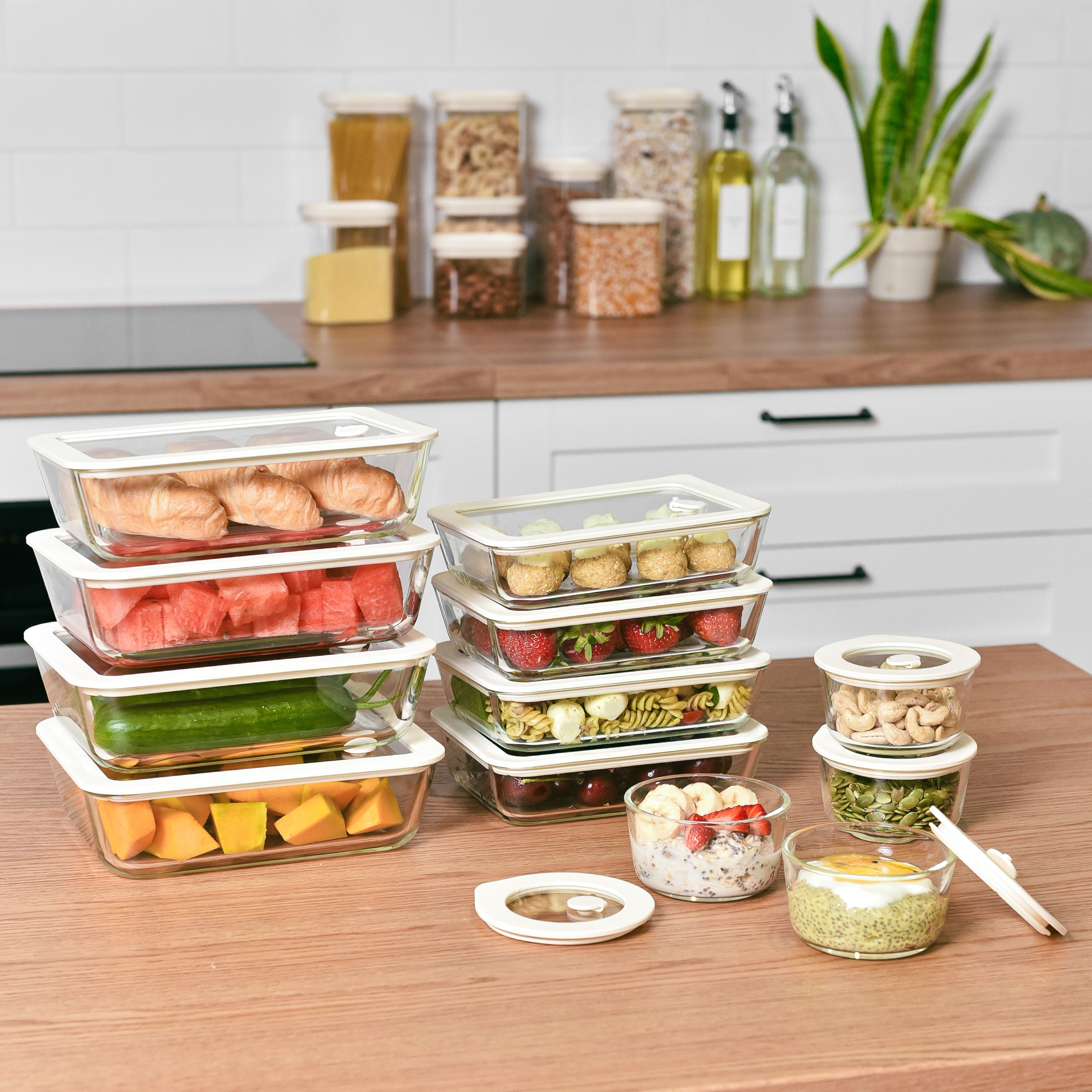 A complete meal prep bundle of glass food storage containers stacked neatly on a wooden kitchen counter.