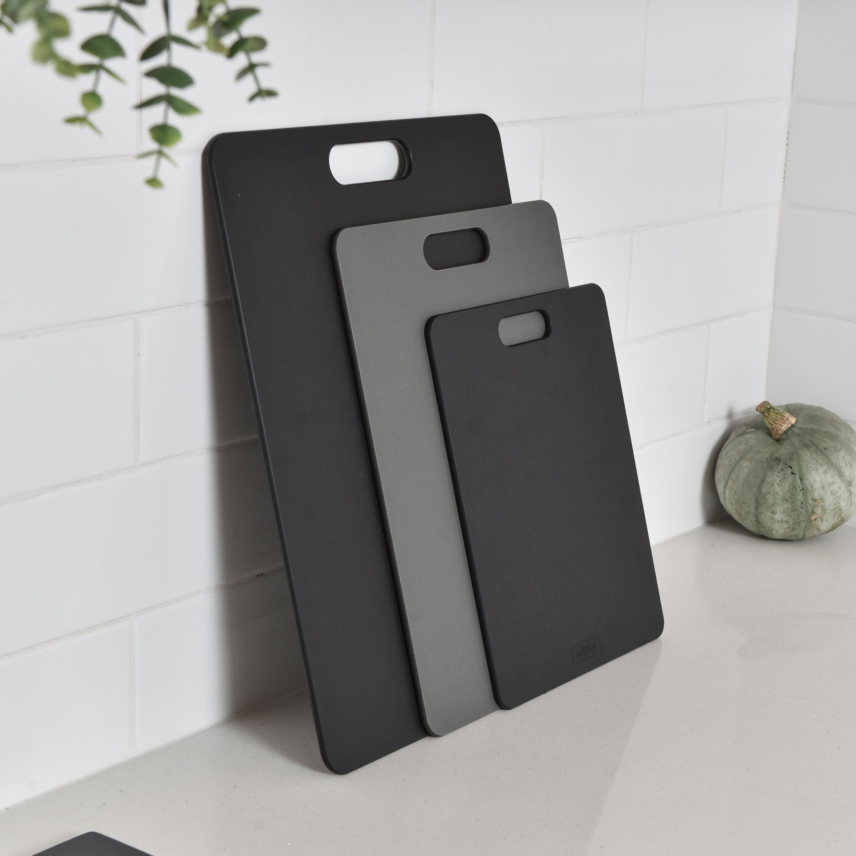 Three wood fibre chopping boards leaning against a kitchen splashback.