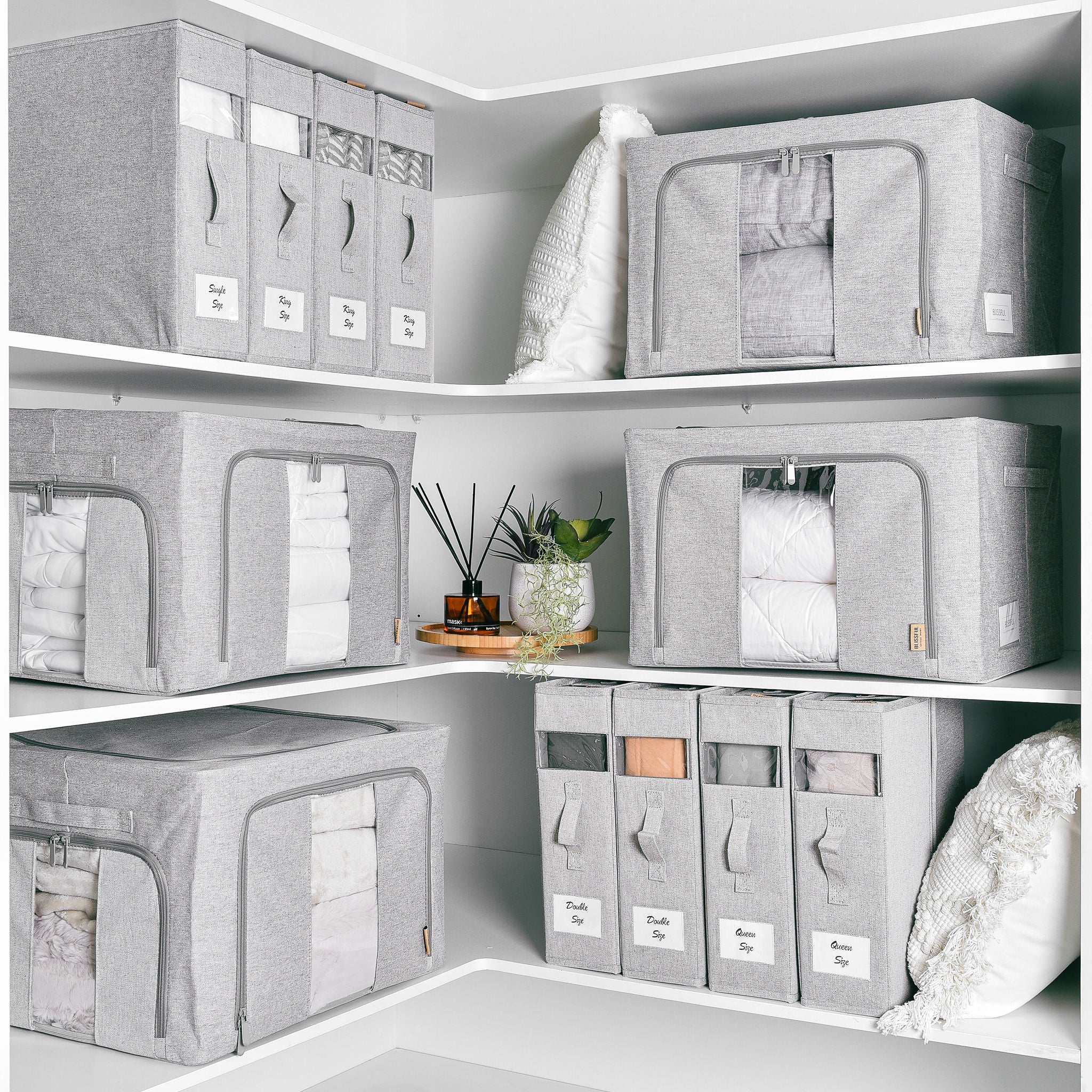 Grey fabric linen storage boxes with clear windows organising a corner cupboard.