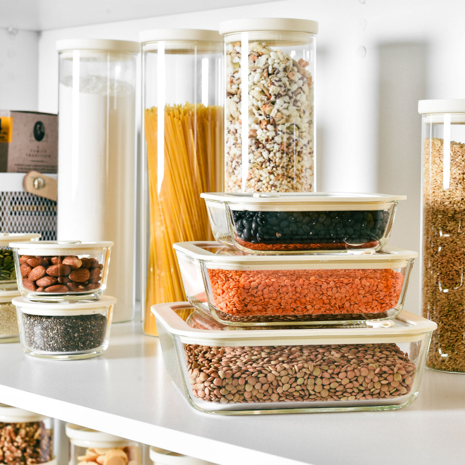 Borosilicate glass kitchen storage containers and jars holding pasta, lentils and dry goods on a warm timber benchtop