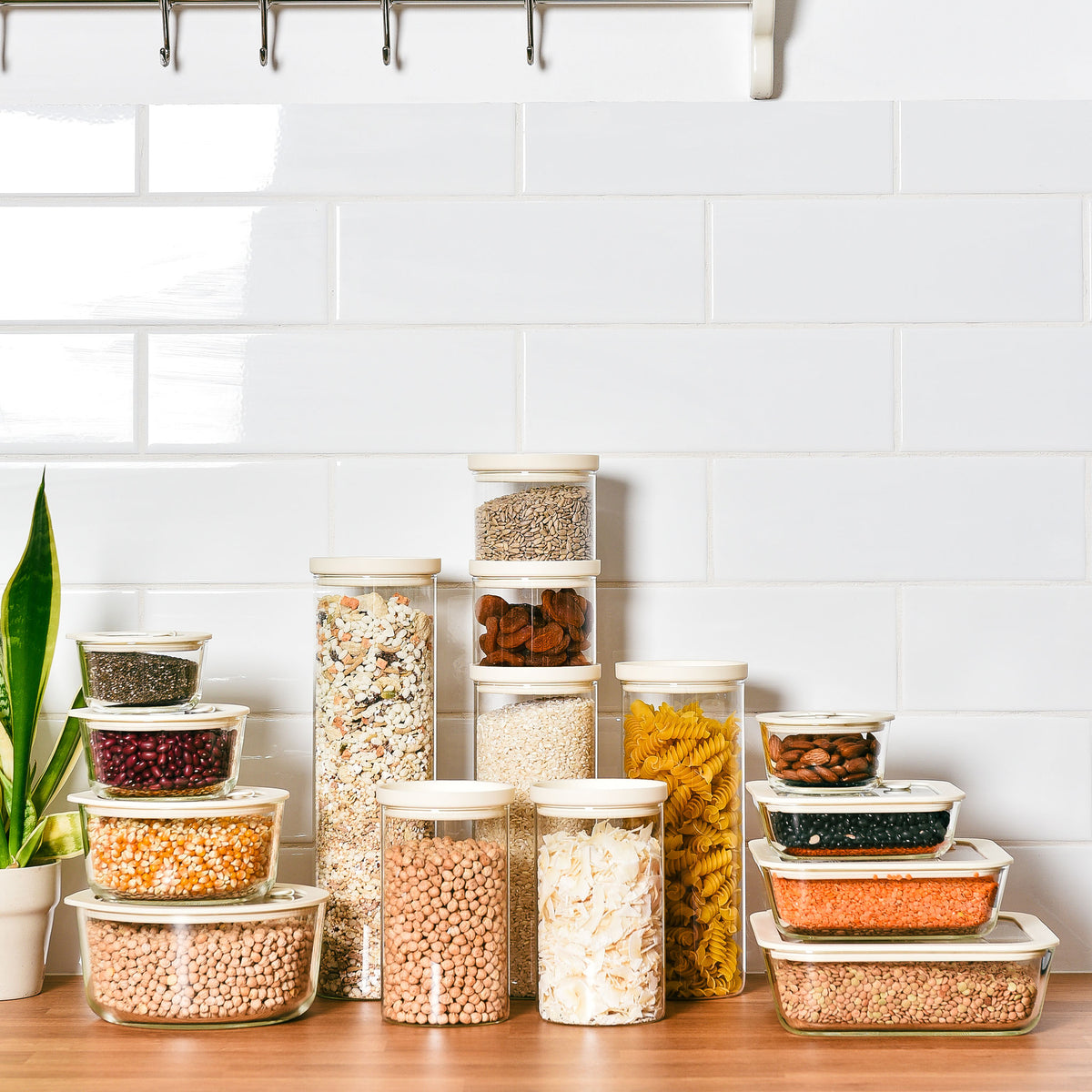 Graduated glass storage jars and food storage containers filled with pasta, oats and dry goods on a timber bench