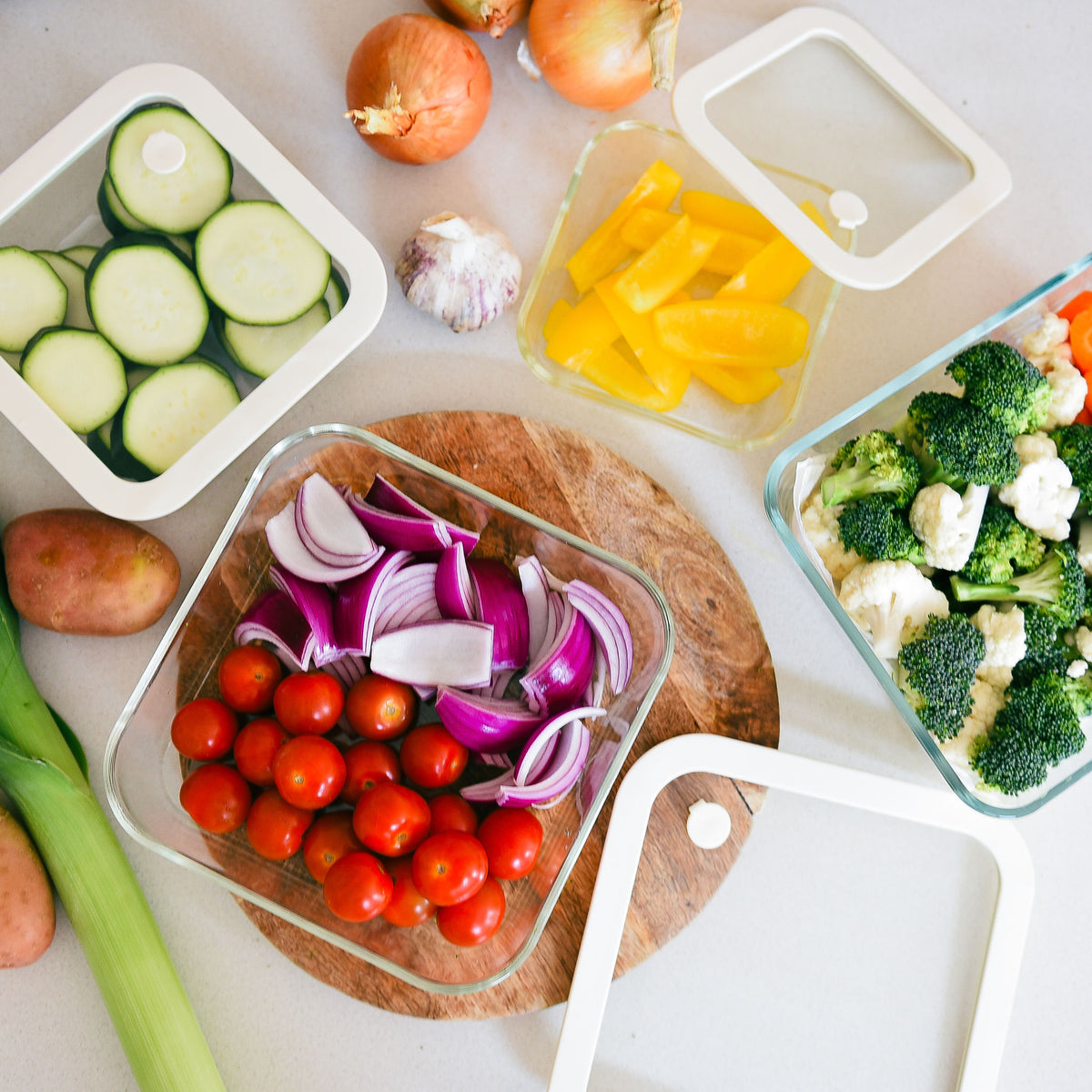 Clear food storage containers filled with chopped vegetables and fresh produce on a kitchen bench